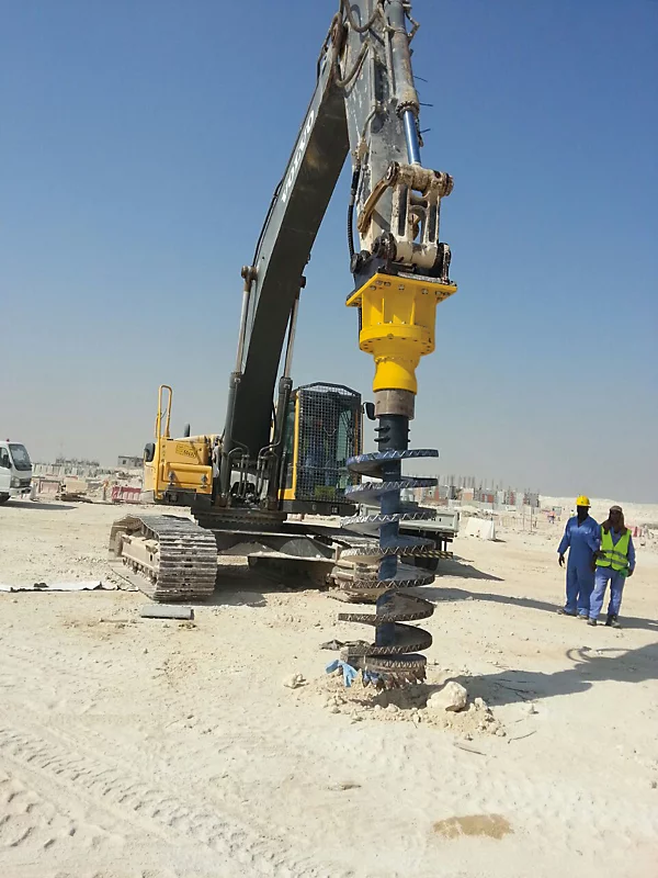 Excavator using an auger drill for construction on site under clear skies.