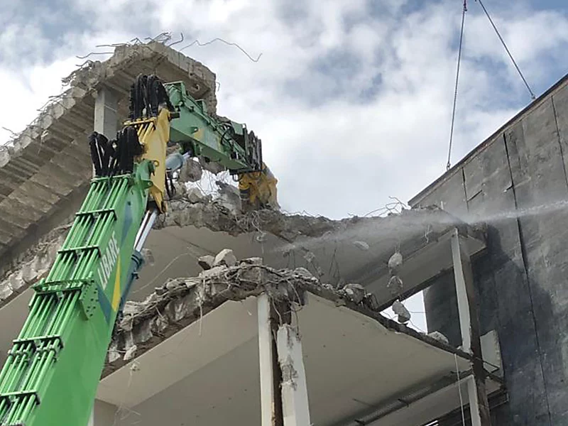 Excavator demolishing a multi-story building with precision, emphasizing efficient demolition services.