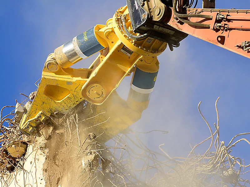 Demolition equipment tearing down a concrete structure against a clear blue sky.