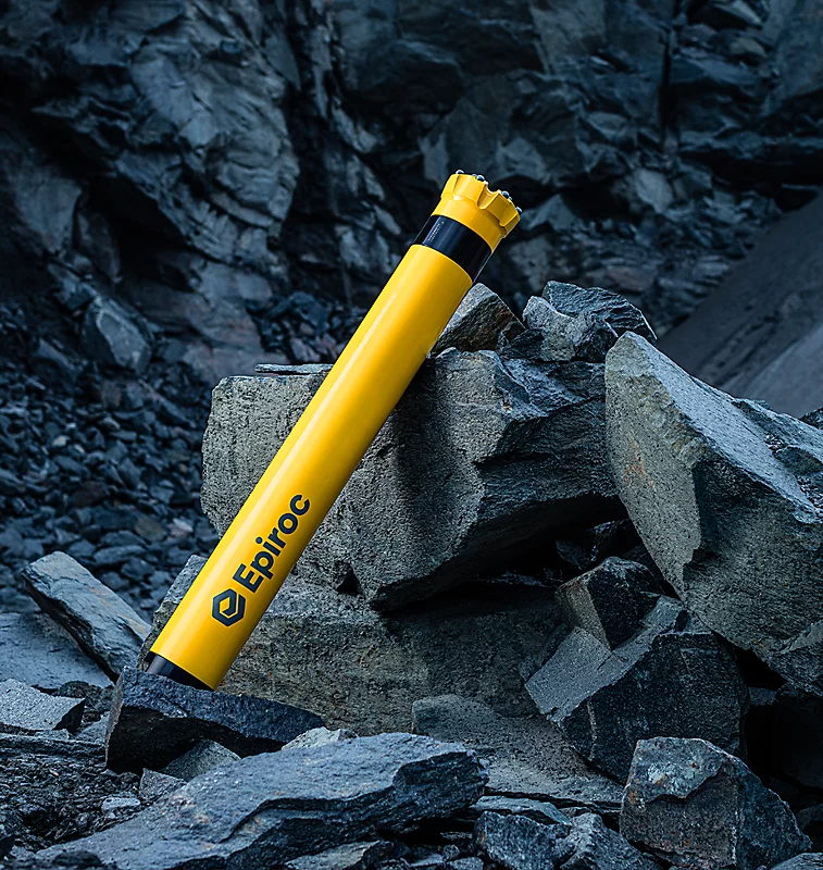 Yellow Epiroc drill pipe on rocky terrain, showcasing durability in mining equipment.