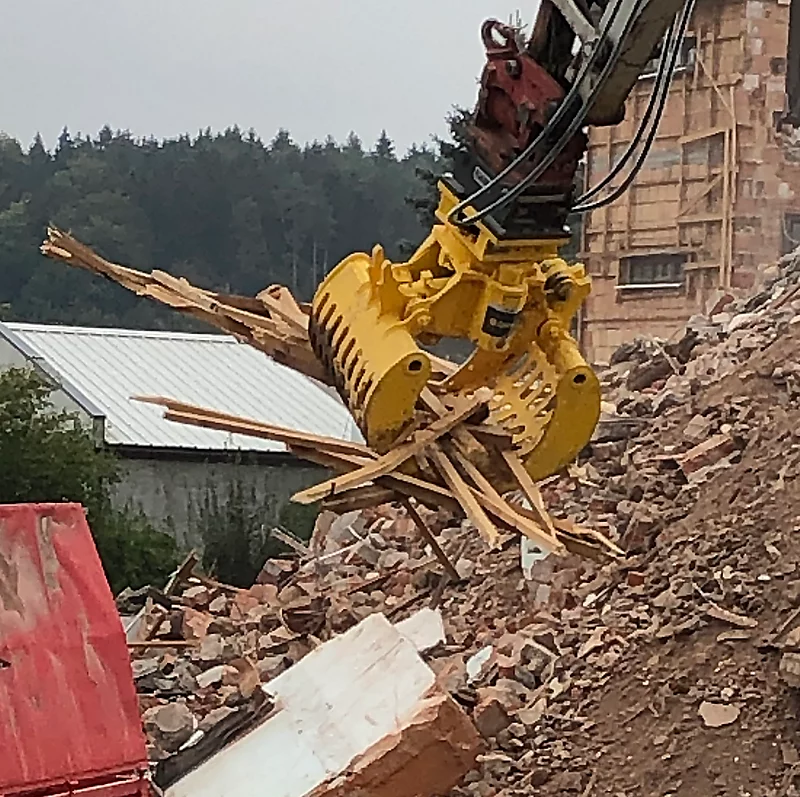 Excavator claw grasping debris on construction site, showcasing demolition process.
