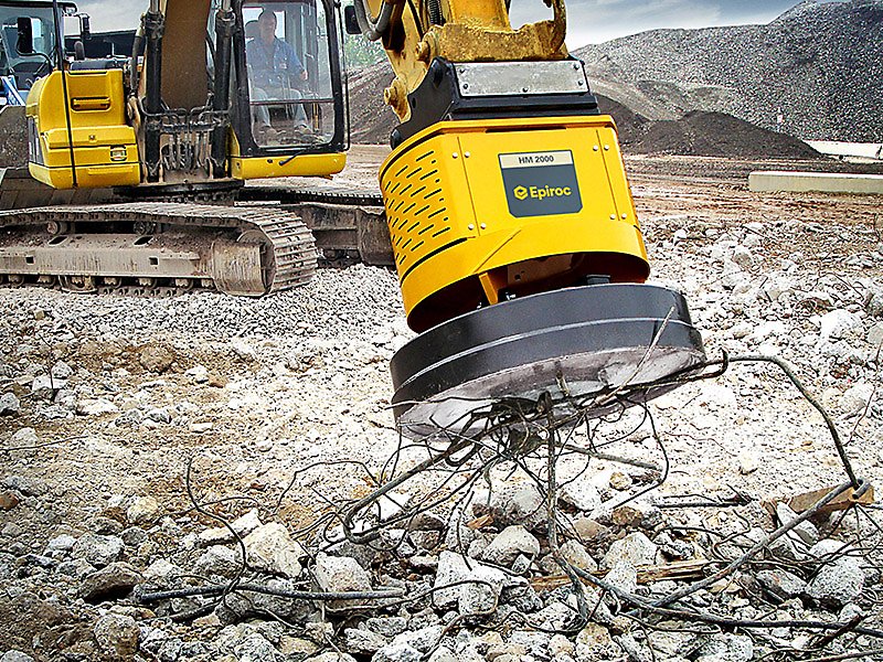 Excavator with Epiroc HM 2000 magnet attachment lifting metal debris on construction site.