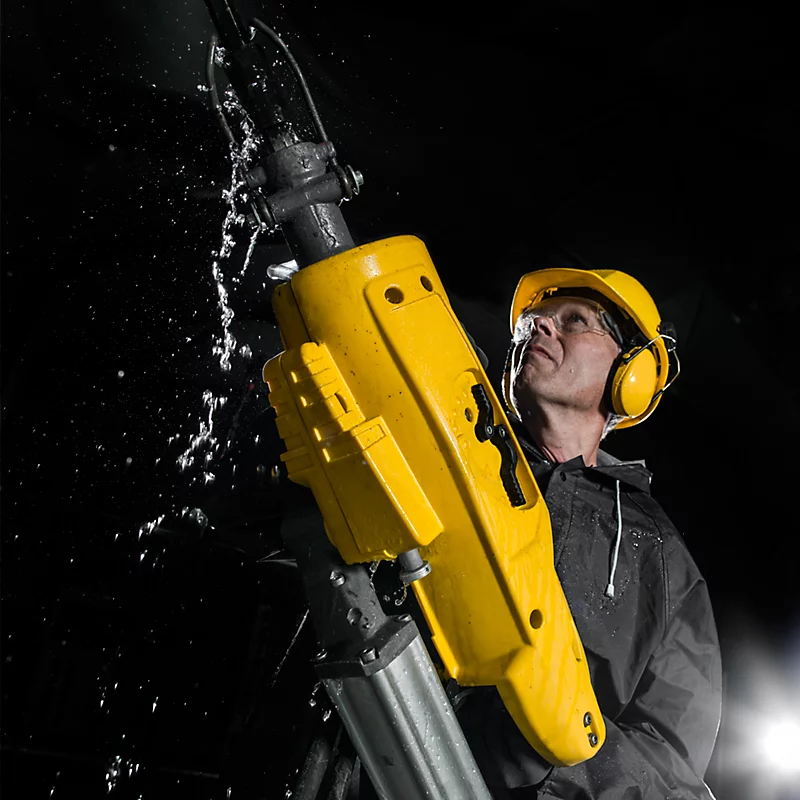 Man in safety gear operating a heavy-duty yellow jackhammer; construction equipment in use.