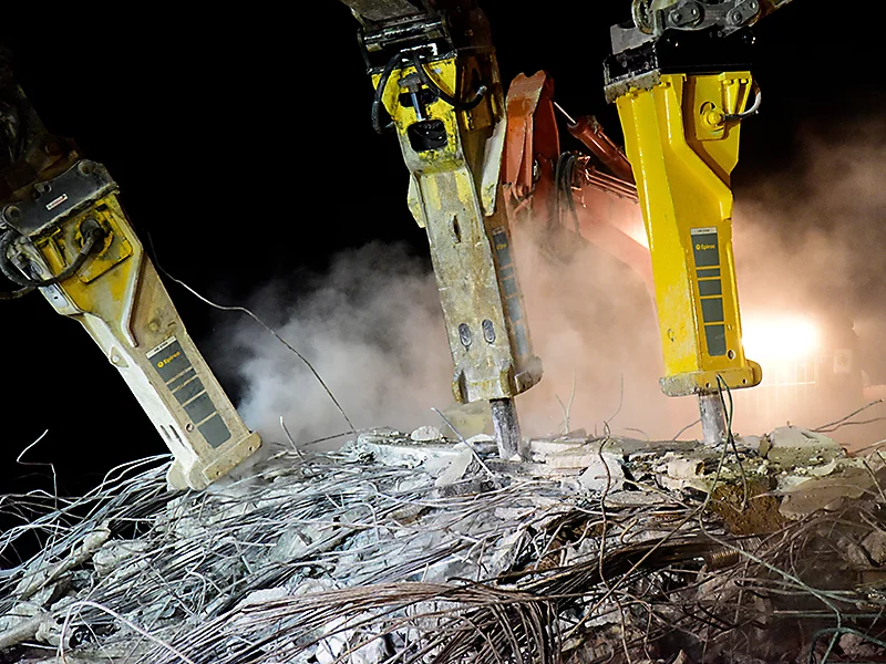 Demolition equipment breaking concrete at night, highlighting efficient construction solutions.
