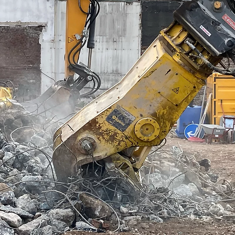 Excavator demolishing concrete, scattering debris at a construction site. Heavy machinery in action.