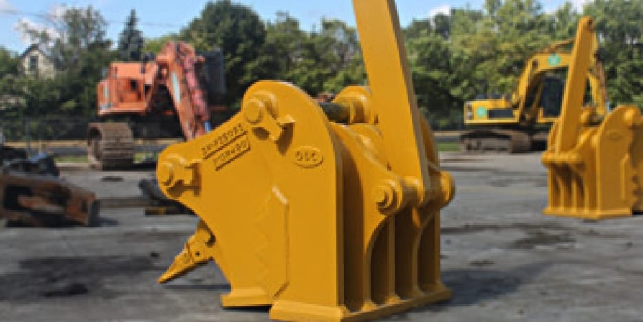 A yellow excavator attachment displayed outdoors, with other construction equipment in the background.