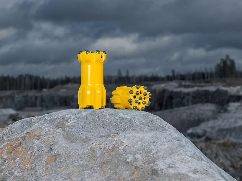 Yellow drilling tools on a rock in a quarry, under a cloudy sky, showcasing durability and precision.